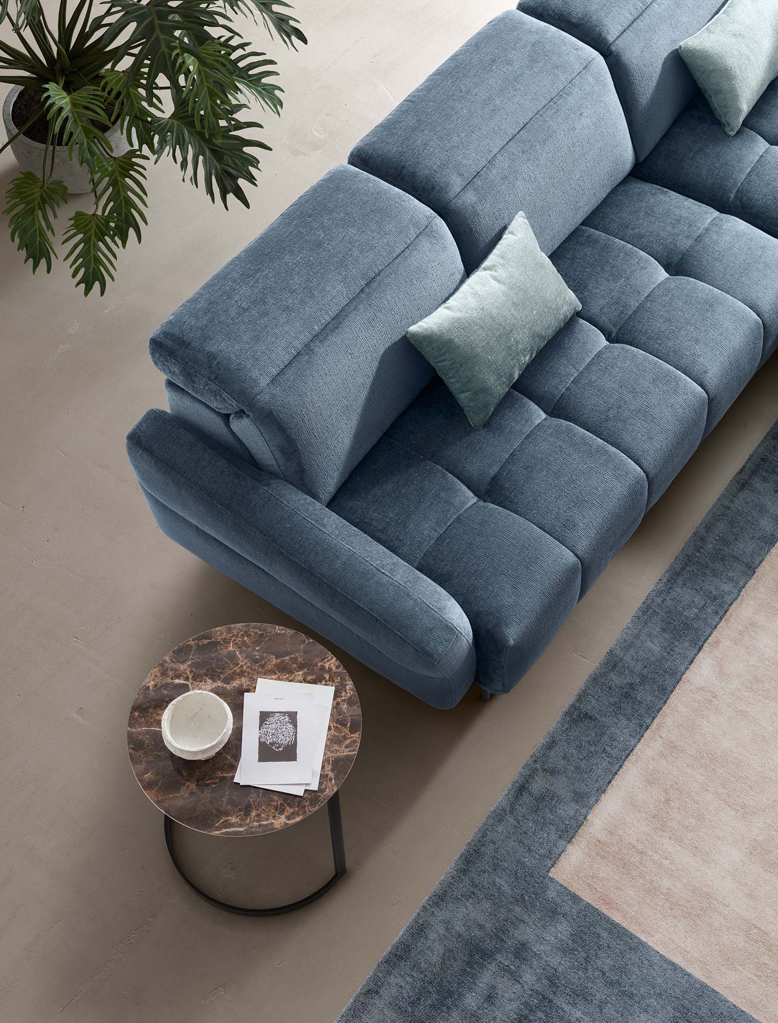 Vista dall'alto del divano Gillan con cuscini azzurri appoggiati alla seduta trapuntata. Design arrotondato.