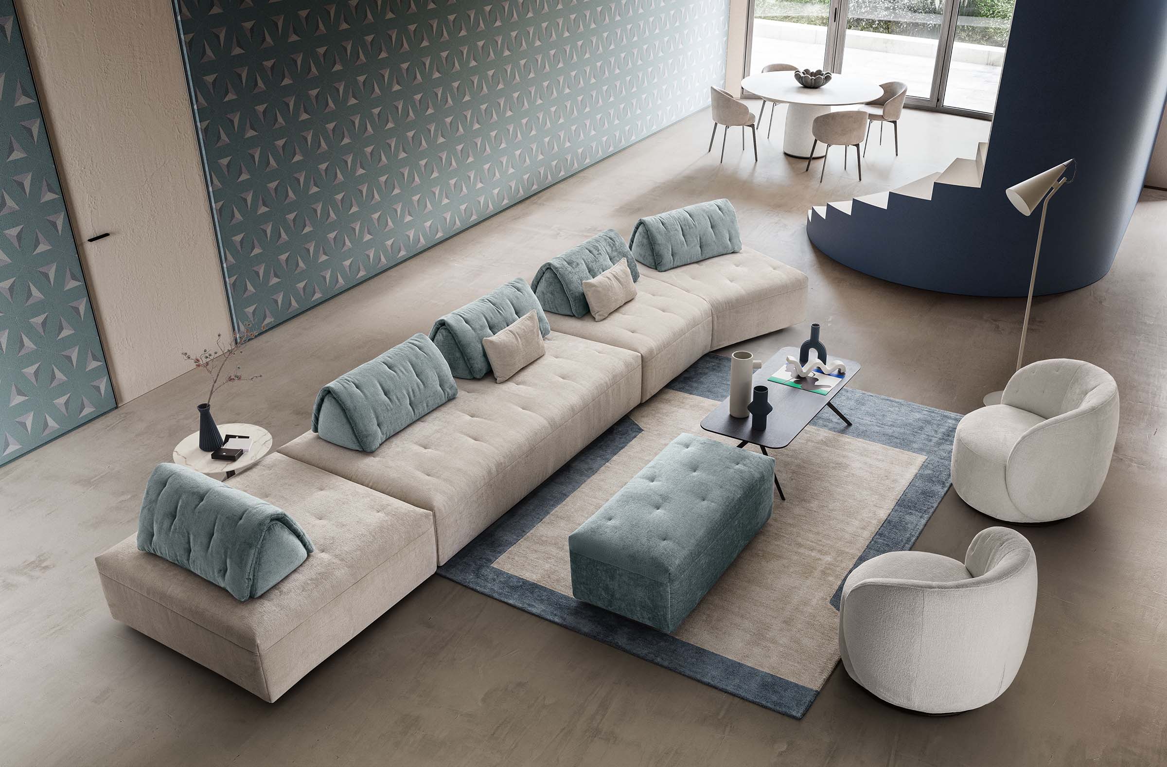 Divano modulare in composizione lineare con seduta asimmetrica laterale. Pouf e poltroncine a completamento