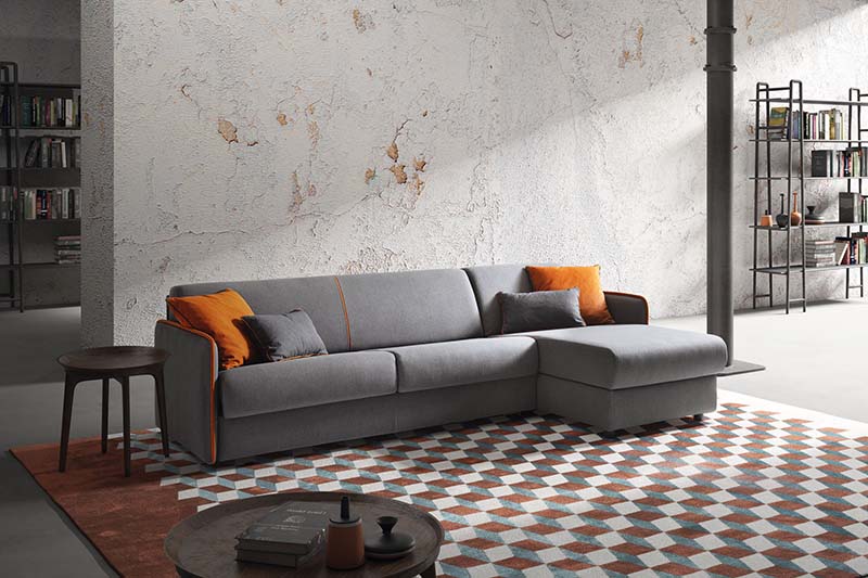 Divano letto con chaise longue laterale. Colore grigio con cuscini arancioni a contrasto