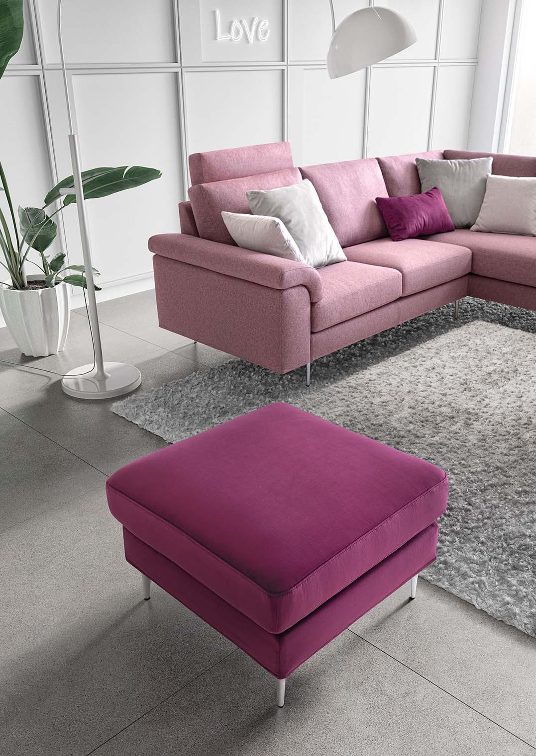 Divano rosa in versione angolare con cuscino poggiatesta aggiunto allo schienale.