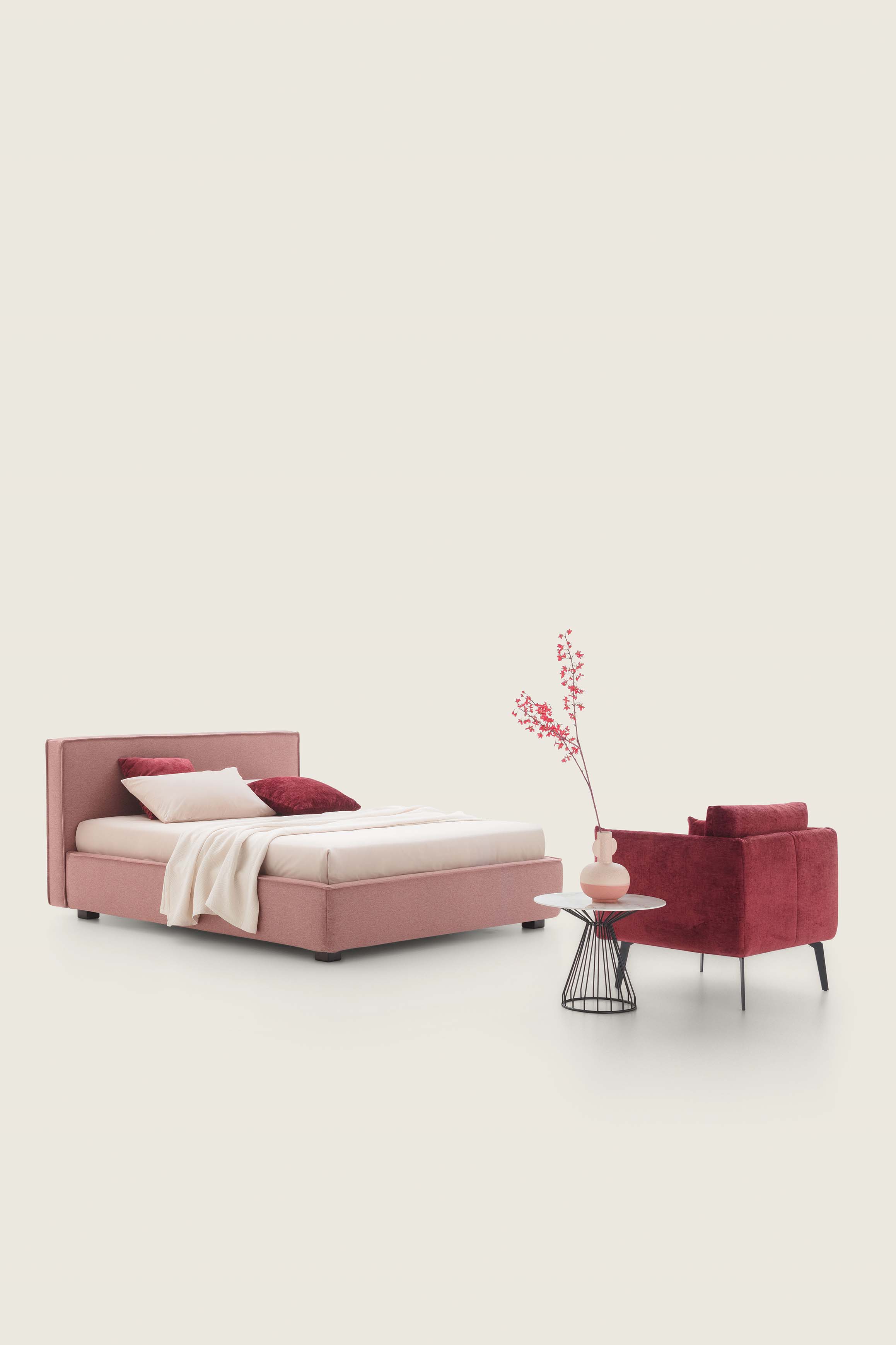 Letto matrimoniale basso color cipria abbinato a una poltrona color bordeaux