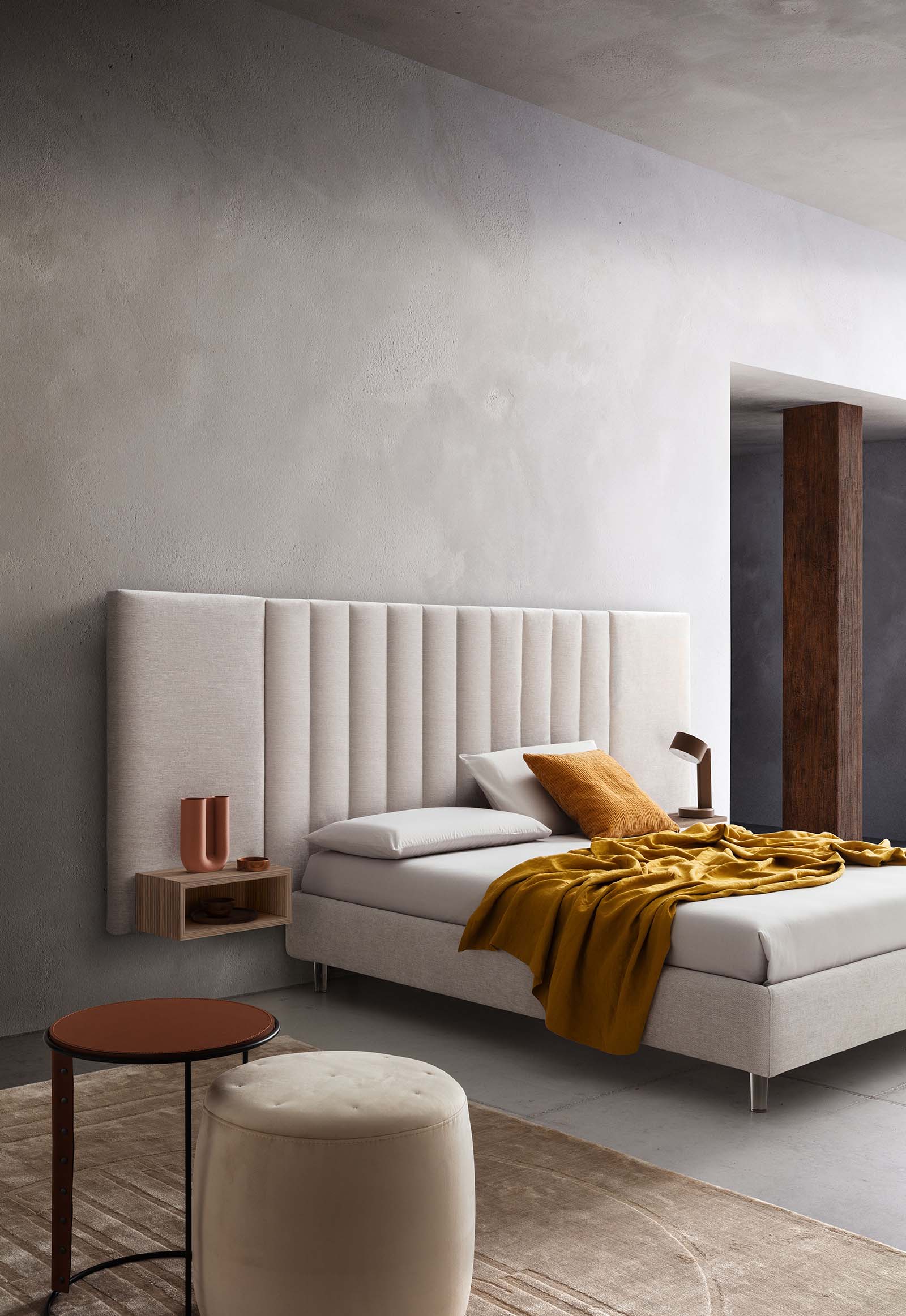 Stanza arredata con letto bianco con piedini in vetro e testiera ampia imbottita con trapuntature verticali